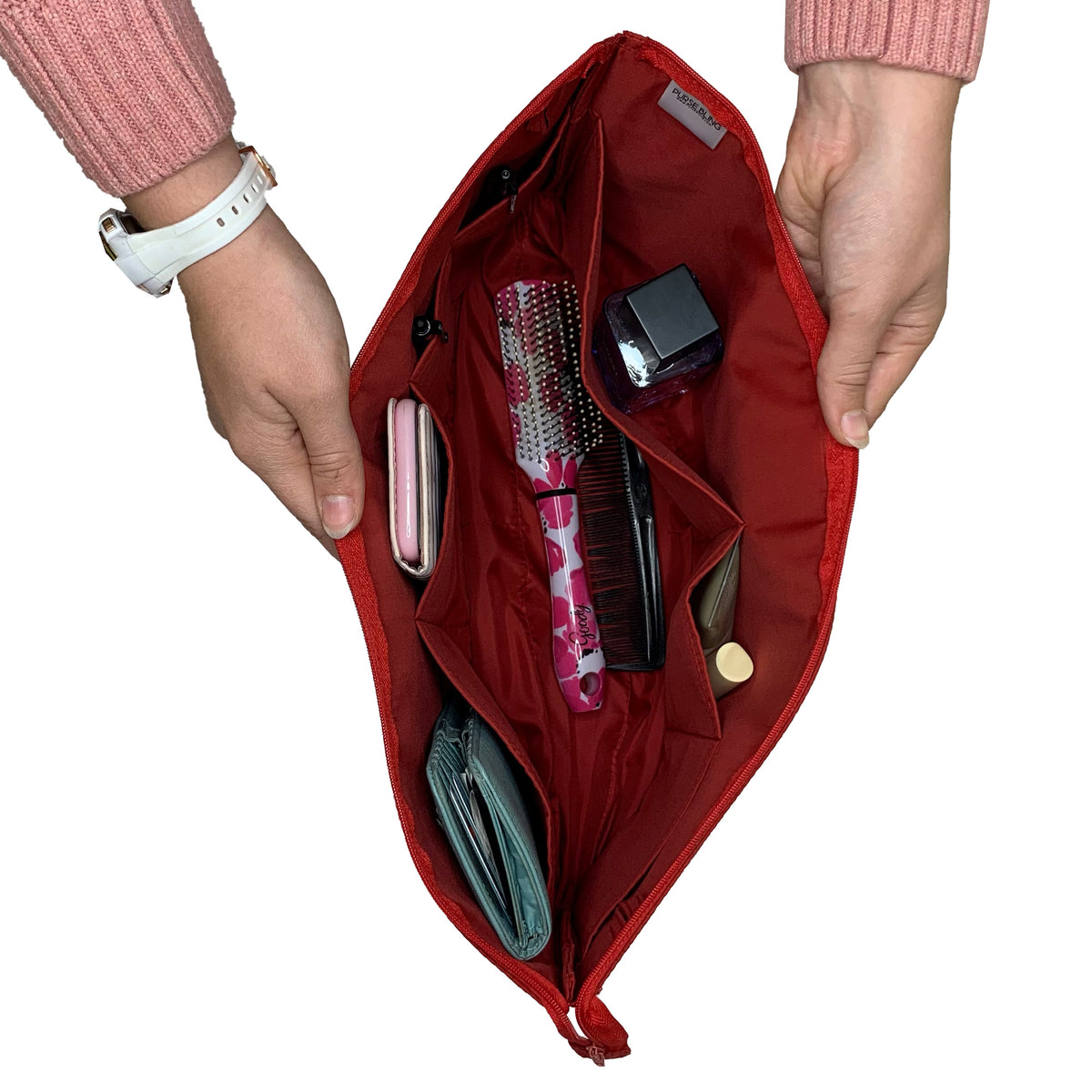 Hands holding an open Purse Bling Slim Purse Organizer Insert with Zipper - Large, featuring various items inside such as a patterned brush, compact powder, wallet, and phone. The high-quality zipper ensures everything remains secure within the polyester/nylon compartments.