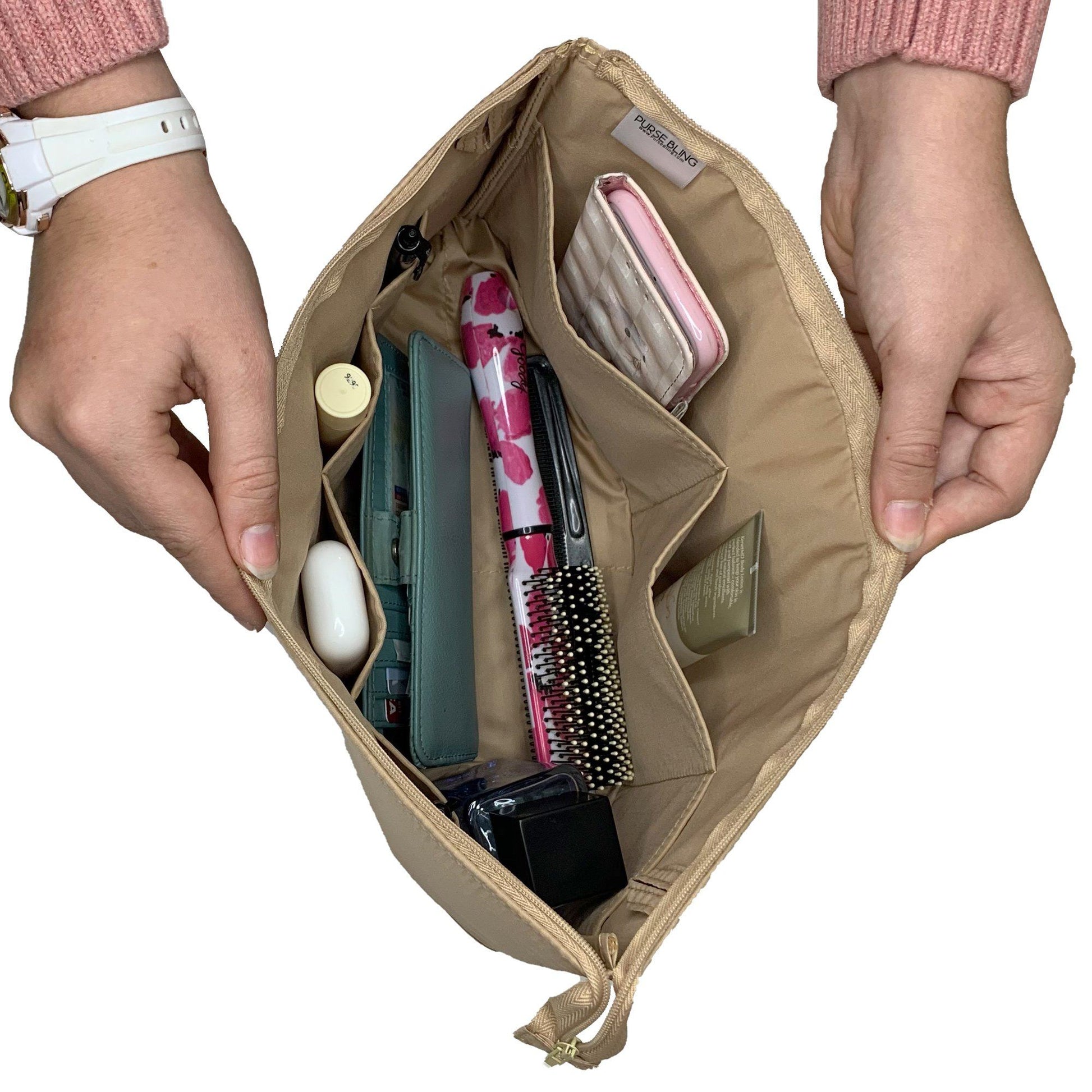 A person holds the Purse Bling Slim Purse Organizer Insert with Zipper - Jumbo, in a beige color, made from durable polyester nylon and packed with essentials such as a pink umbrella, wallet, brush, lipstick, card holder, and more. It includes a high-quality zipper to keep everything securely in place.